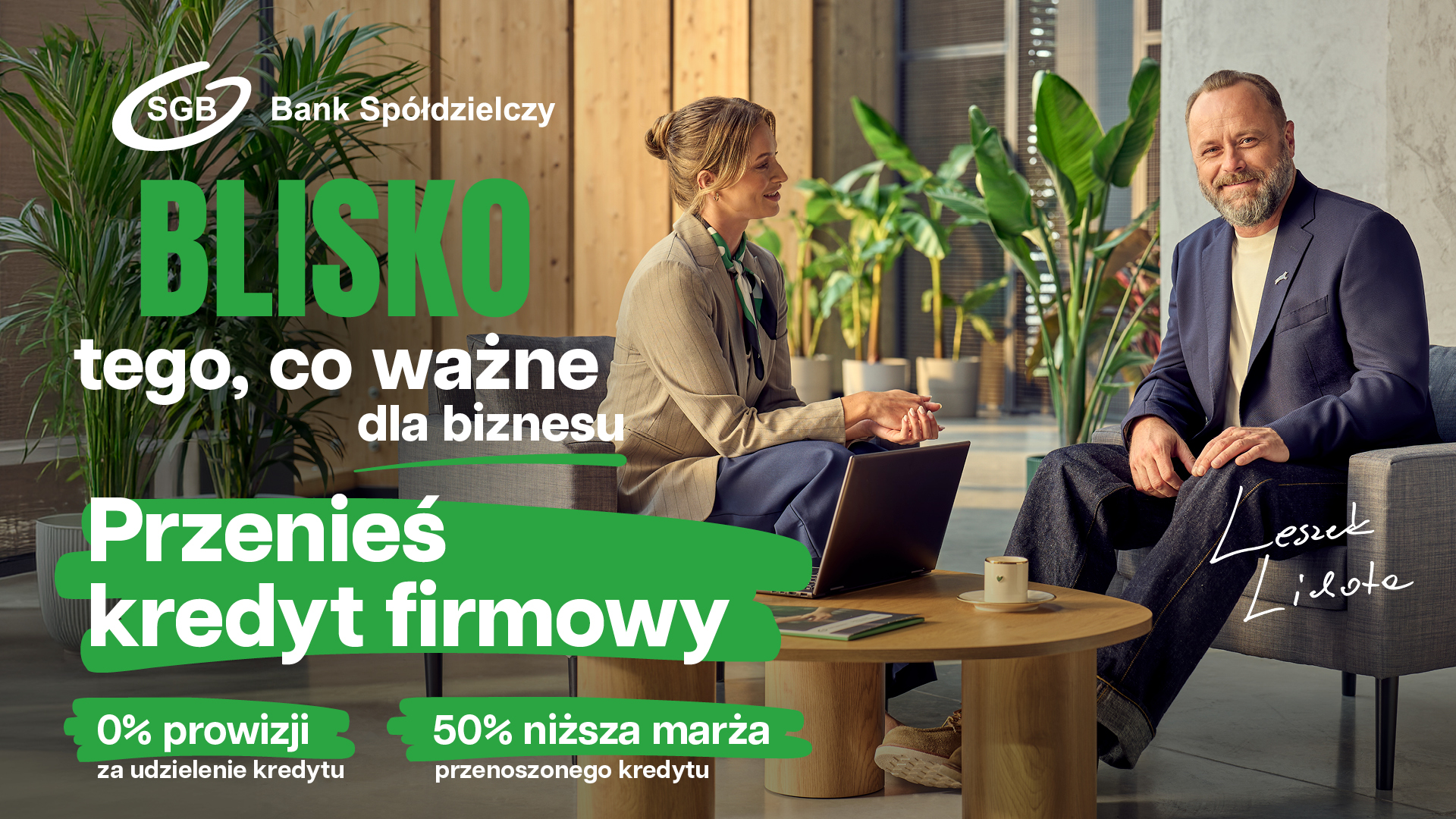 W nowoczesnym biurze siedzi mężczyzna w garniturze i kobieta w stroju biznesowym. W tekście reklamowym mowa jest o przeniesieniu kredytu biznesowego z 0% prowizją i o 50% niższym marżem.