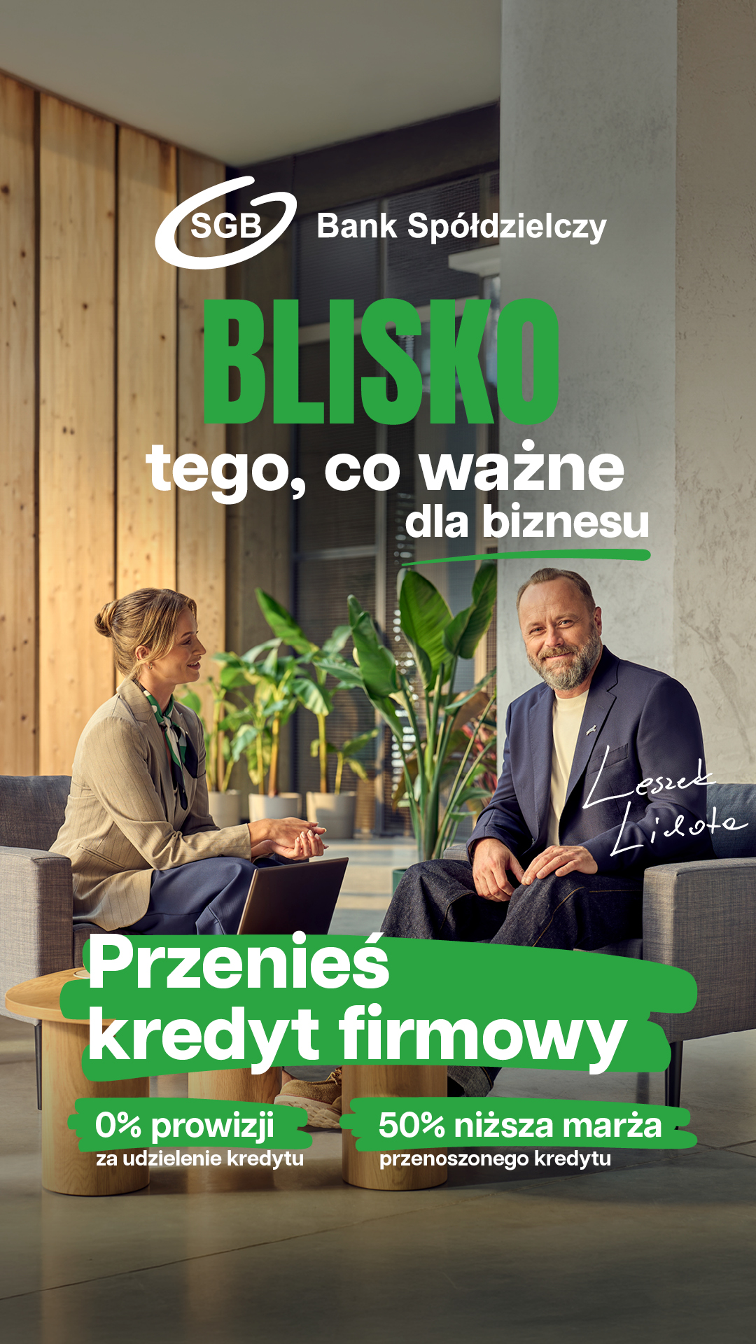Dwie osoby siedzą na krzesłach w nowoczesnym biurze z roślinami. Tekst w języku polskim promuje kredyty biznesowe bez prowizji i z obniżonym oprocentowaniem oferowane przez SGB Bank Spółdzielczy.